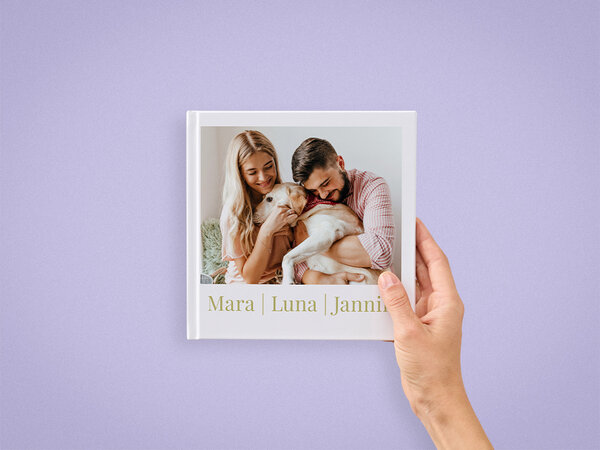 Ein Fotobuch im Format 20x20 wird von einer Hand gehalten. Auf dem Cover ist ein Paar mit ihrem Hund zu sehen.