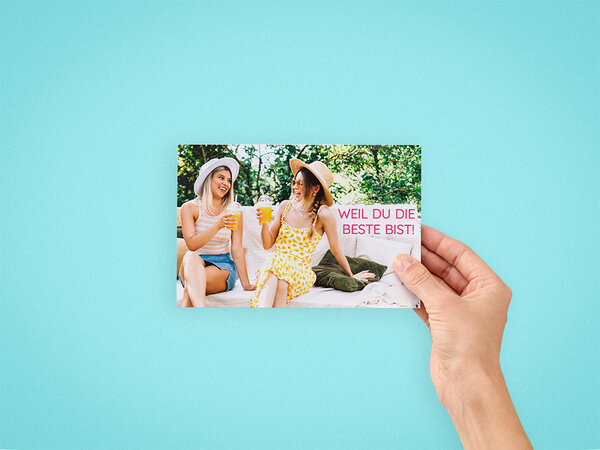 Mit der rechten Hand wird ein querformatiges Fotobuch gehalten. Auf dem Cover sind zwei Freundinnen abgebildet.