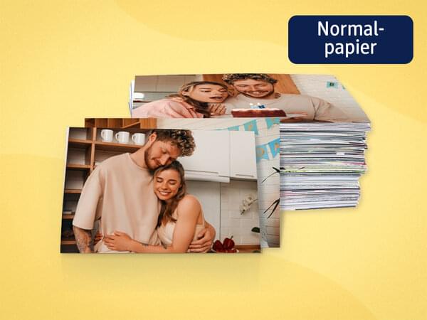 Zwei Fotoabzüge mit Bildern von einem Paar sind angelehnt an einen Stapel voller Fotoabzüge.