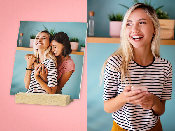 Mehrere quadratische Fotos stehen frei in einem Holzstandfuß. Das vorderste Foto zeigt zwei Frauen, die sich umarmen.