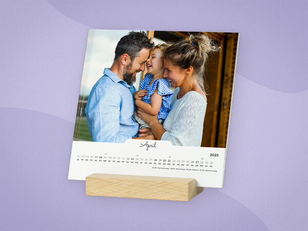 Quadratische Kalenderblätter stehen frei in einem Holzstandfuß. Kalender hat weißes Design, mit Familienfoto.